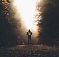 Person mit Rucksack auf einem Waldweg im Morgenlicht