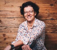 Über mich – Iris Determann | Coaching, Mediation und persönliche Entwicklung Portrait von Iris Determann vor einer Holzwand mit freundlichem Lächeln